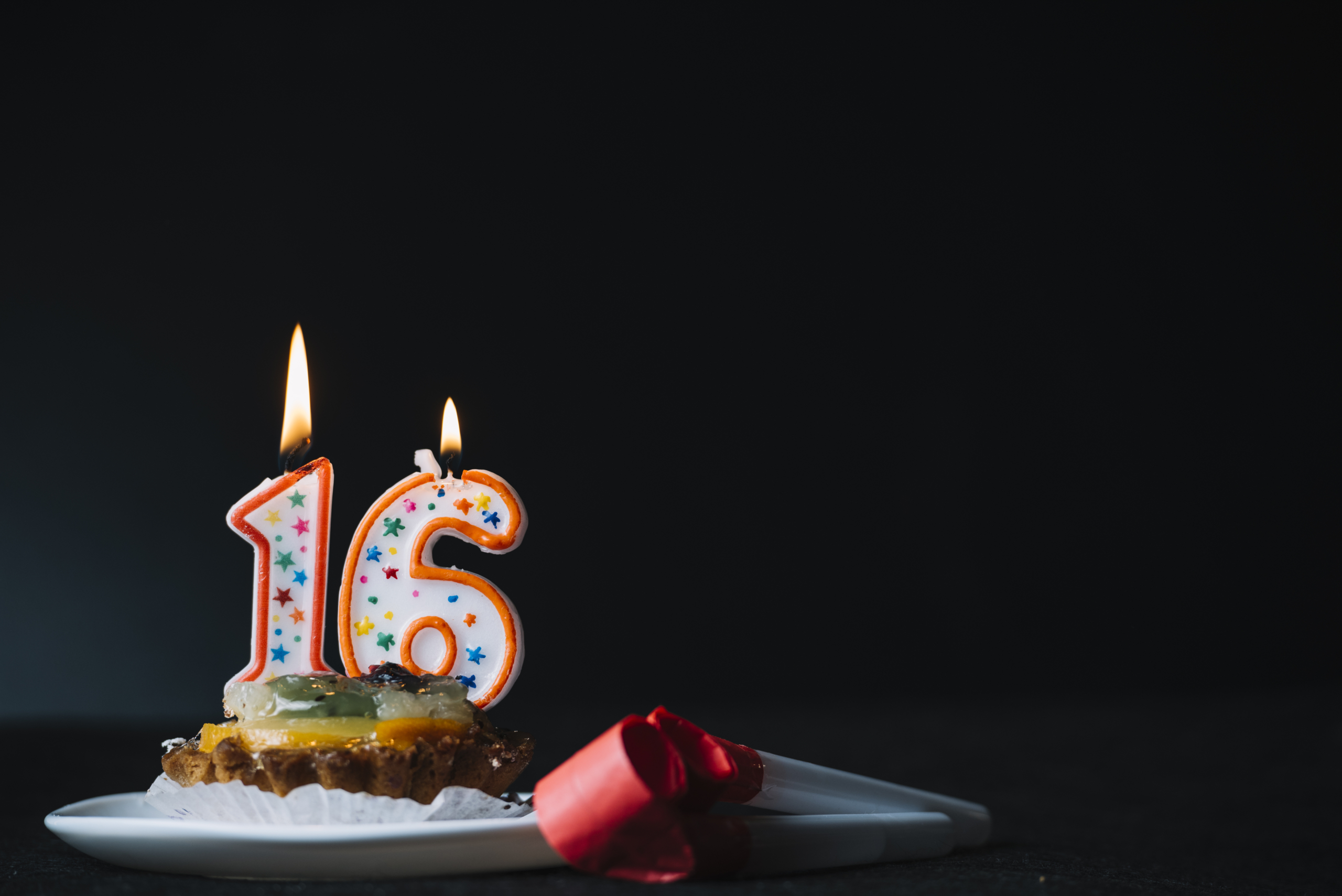 Number 16 candle on cake slice with party blower, against black background. Child Marriage in Barbados