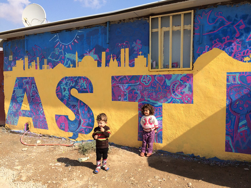 Group of people viewing vibrant mural; part of refugee art initiatives.