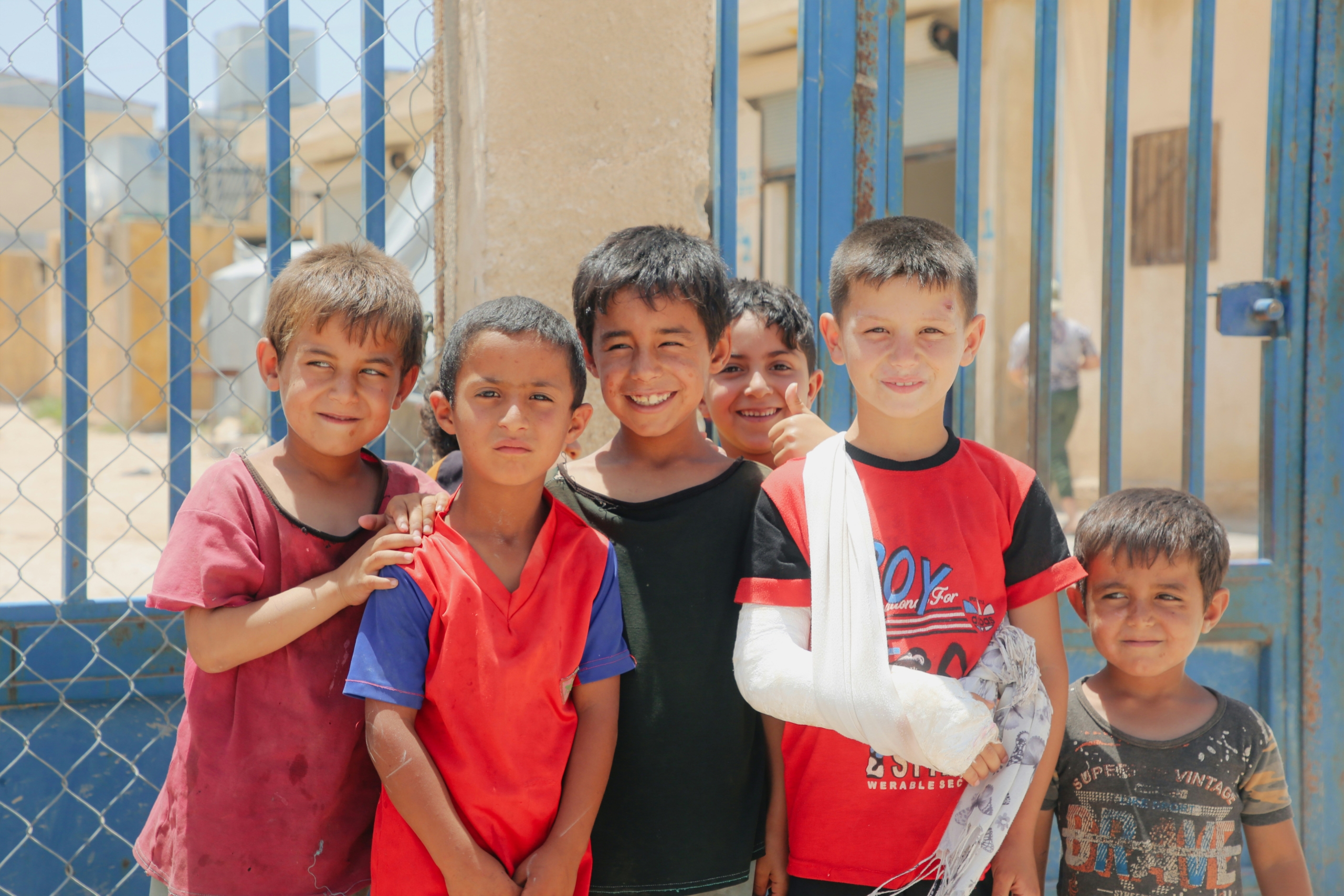 A group of young boys standing together, smiling outdoors. GCC Humanitarian Aid