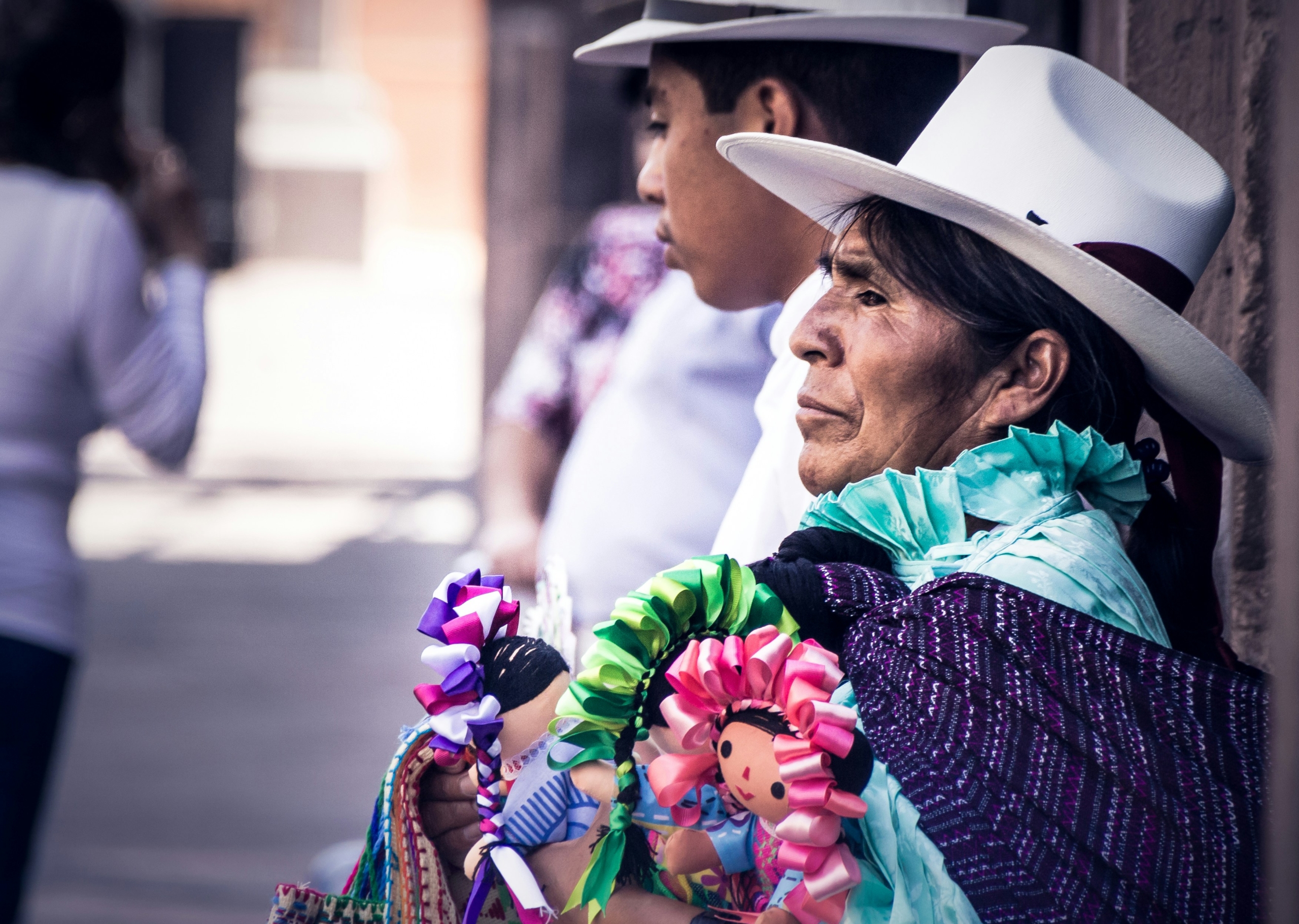 Woman in colorful clothing stands against a gray wall, reflecting Indigenous culture. Indigenous Migrants in Mexico City