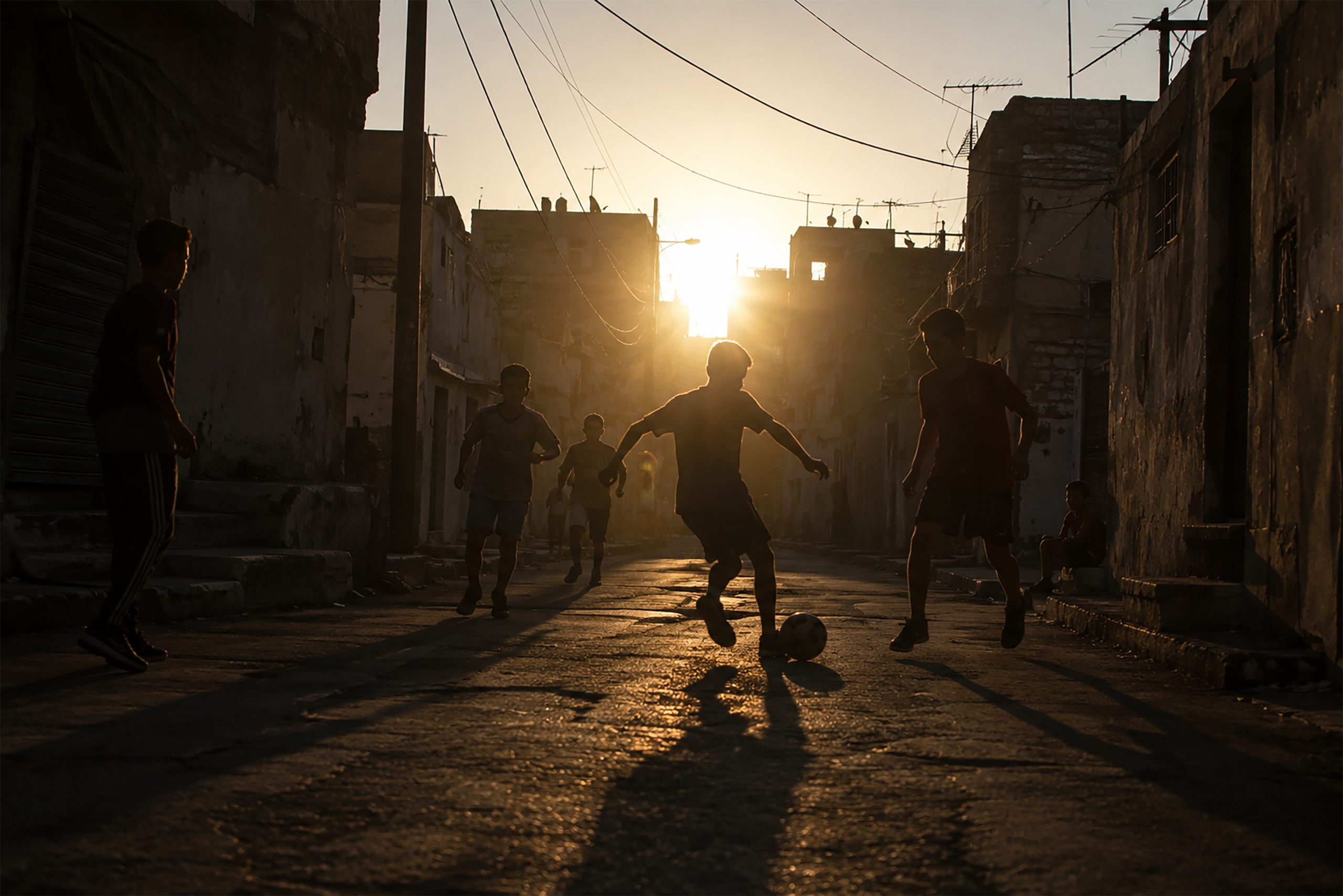 Silhouette of a child playing soccer at sunset on a street. World Cup Soccer Players Who Grew Up in Poverty